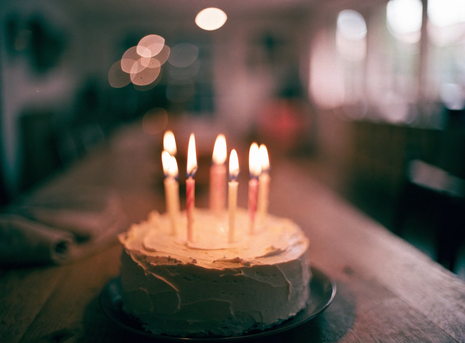 A birthday cake with lit candles on a wooden table in warm candlelight