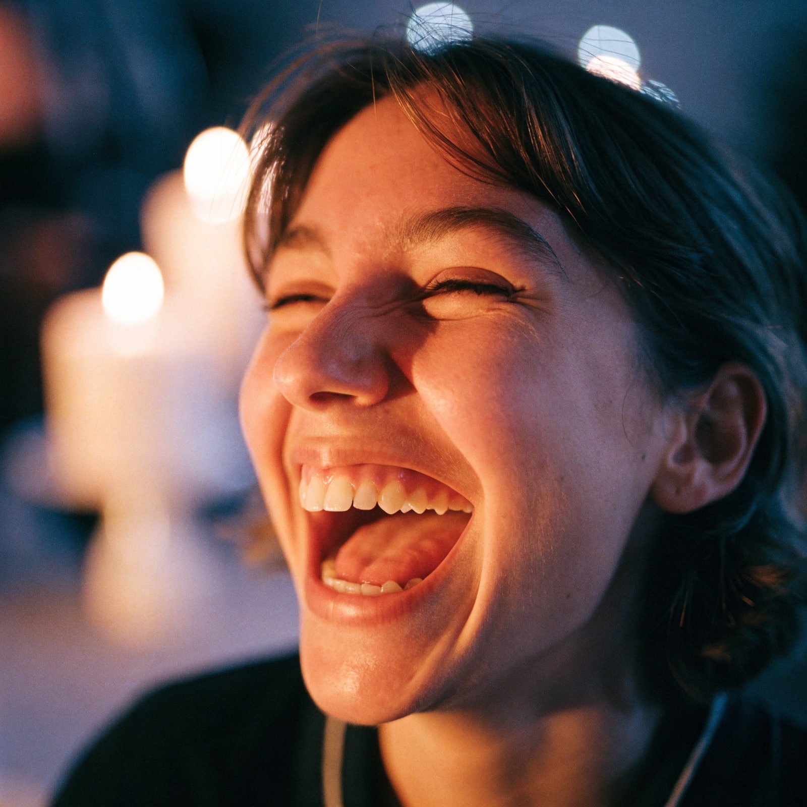 A young woman laughing with joy at her birthday, candlelight glowing on her face