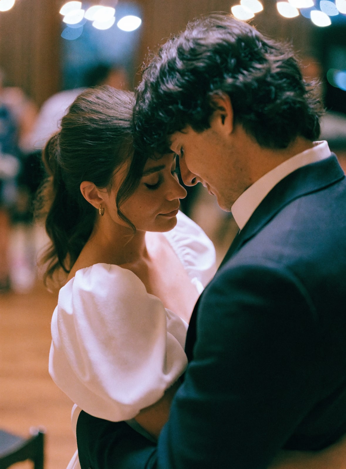 A couple's first dance at a wedding reception under warm fairy-light bokeh
