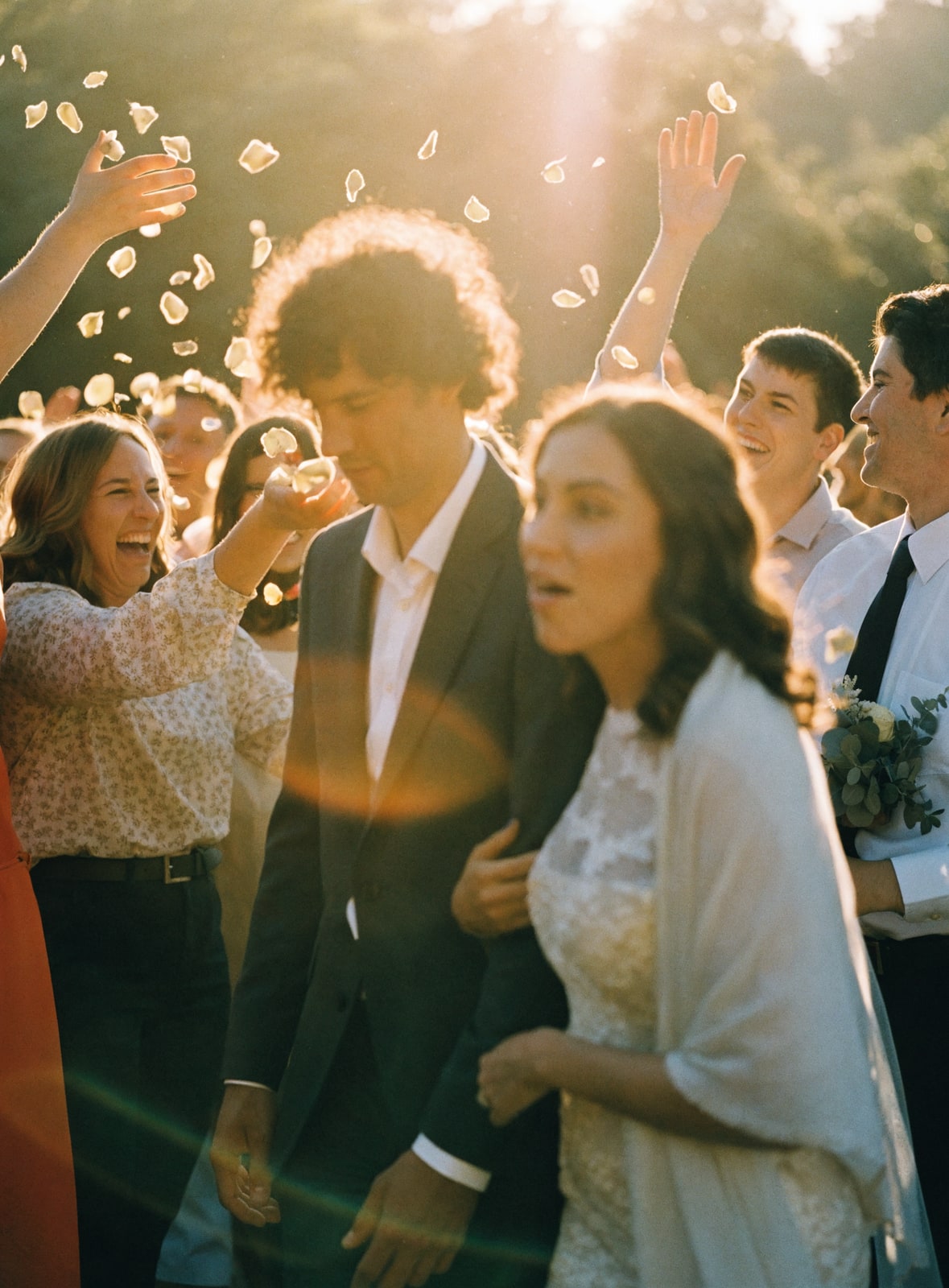 A golden-hour wedding send-off, guests tossing flower petals as the couple walks